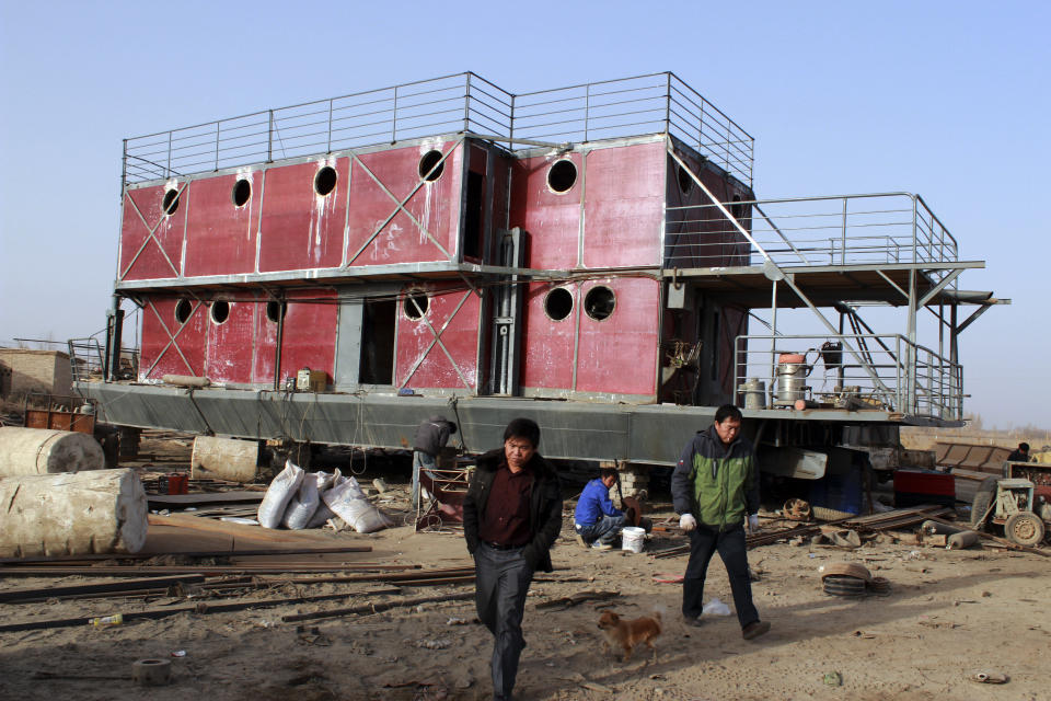 In this photo taken Nov. 24, 2012, Lu Zhenghai, right, walks near his ark-like vessel in China's northwest Xinjiang Uyghur Autonomous Region. Lu Zhenghai is one of at least two men in China predicting a world-ending flood, come Dec. 21, the fateful day many believe the Maya set as the conclusion of their 5,125-year long-count calendar. Zhenghai has spent his life savings building the 70-foot-by-50-foot vessel powered by three diesel engines, according to state media. In Mexico's Mayan heartland, nobody is preparing for the end of the world; instead, they're bracing for a tsunami of spiritual visitors. (AP Photo/ANPF-Chen Jiansheng)