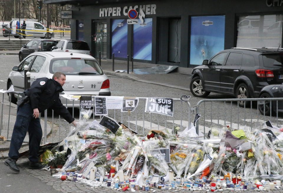 FILE - In this Jan. 12, 2015 file photo, a police officer lays flowers at the site of the kosher market where four hostages were killed and shortly before Israeli Prime Minister Benjamin Netanyahu's visit to the site, in Paris. The January 2015 attacks against Charlie Hebdo and, two days later, a kosher supermarket, touched off a wave of killings claimed by the Islamic State group across Europe. Seventeen people died along with the three attackers. Thirteen men and a woman accused of providing the attackers with weapons and logistics go on trial on terrorism charges Wednesday Sept. 2, 2020. (AP Photo/Francois Mori, File)