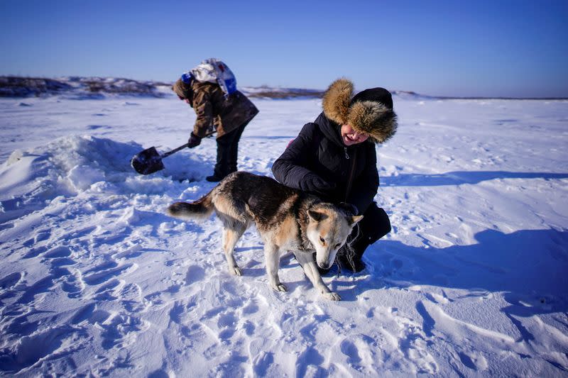 You Wenfeng, 68, an ethnic Hezhen woman plays with a fisherman's dog at a frozen river in Tongjiang