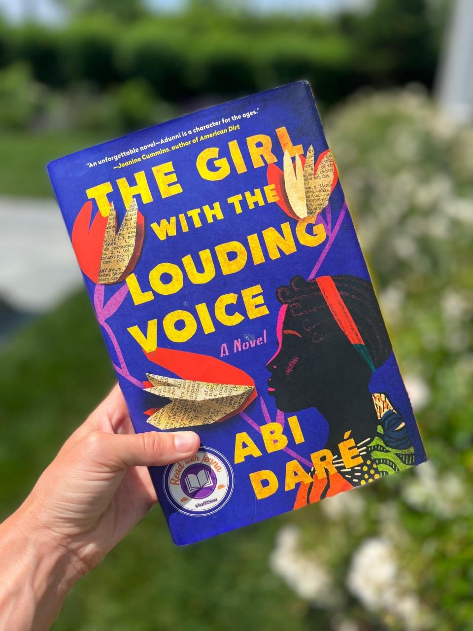 A hand holding "The Girl with the Louding Voice" by Abi Daré.