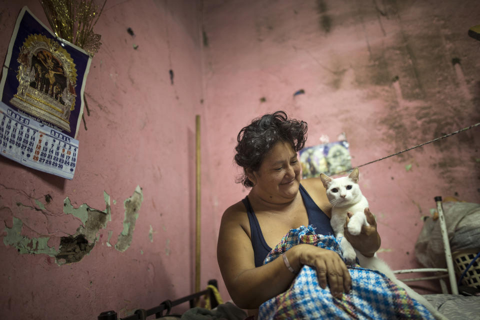 In this April 3, 2020 photo, Zulema Aguinaga smiles at her pet cat as she starts the day inside her small room she shares with her son and elderly aunt, in a deteriorated house nicknamed “Luriganchito,” or “Little Lurigancho,” after San Pedro de Lurigancho, the country’s most populous prison, in Lima, Peru. The government began enforcing strict new measures to curb the spread of the new coronavirus, restricting public movement by gender. Women are allowed to go out on Tuesdays, Thursdays and Saturdays. (AP Photo/Rodrigo Abd)