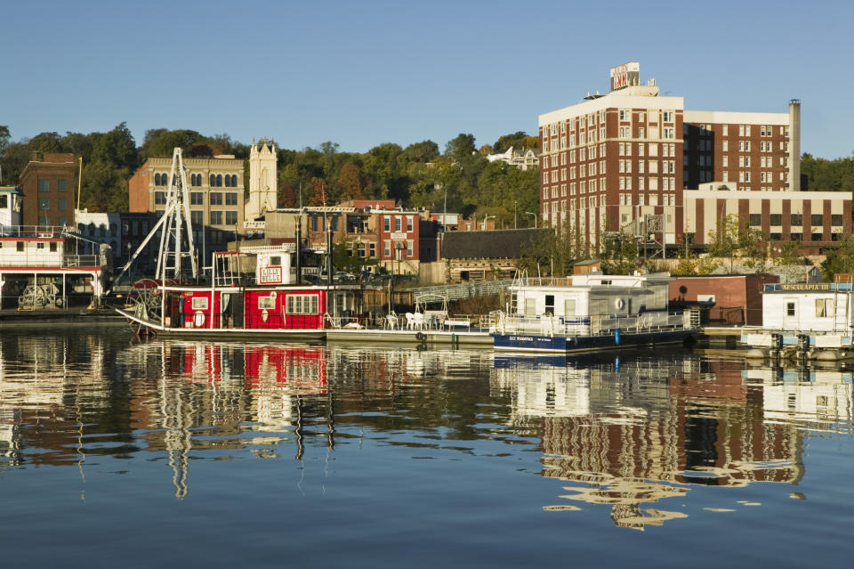 Waterfront scene with docked houseboats and a reflection of the buildings, including an adjacent red brick structure, on the calm water surface