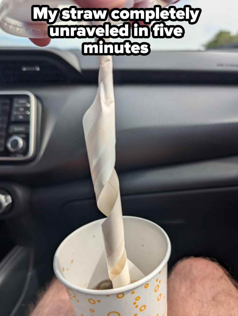 A hand holding a lid with a twisted straw, hovering over a cup in a car interior