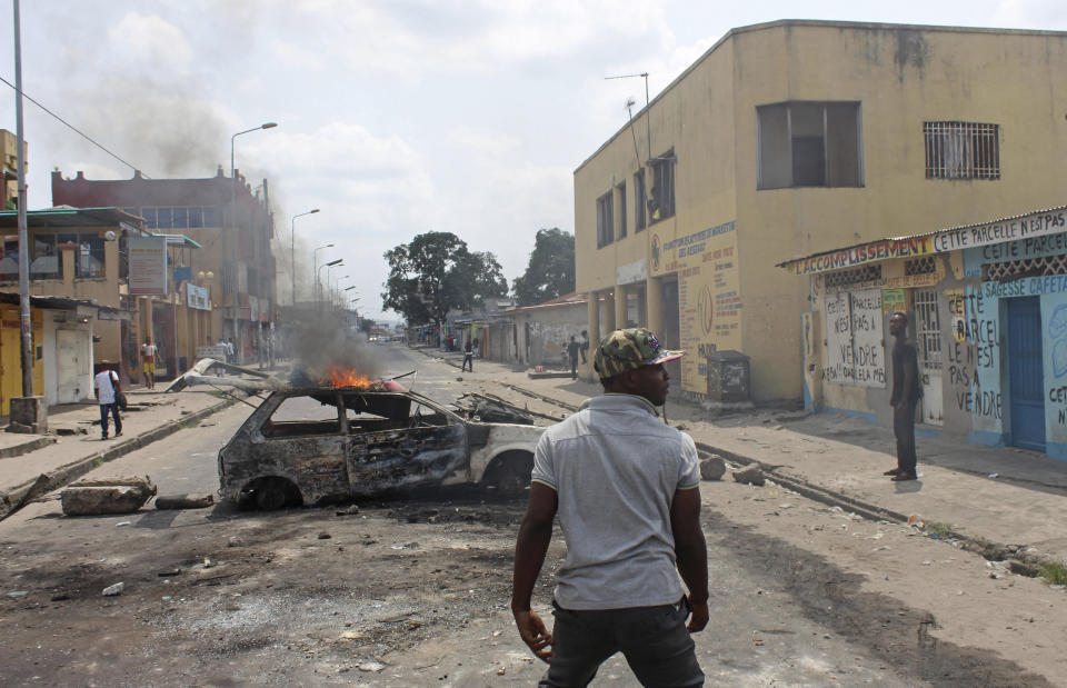 FILE - In this Jan. 20, 2015 file photo shot by AP contributing photographer John Bompengo, an anti-government protestor, center, stands in front a burning car as he and others block roads and burn tires, during a protest against a new law that could delay election to be held in 2016, in Kinshasa, Democratic Republic of Congo. Relatives say longtime Associated Press contributor John Bompengo has died of COVID-19 in Congo's capital. Bompengo, who had covered his country's political turmoil over the course of 16 years, died Saturday, June 20, 2020 at a Kinshasa hospital. (AP Photo/John Bompengo, file)