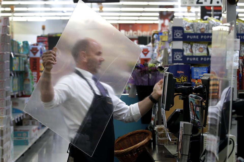 FILE - In this March 26, 2020, file photo, Dave Herrick installs a plexiglass panel at a checkout lane at a Hy-Vee grocery store in Overland Park, Kan. Grocery workers across the globe are working the front lines during lockdowns meant to keep the coronavirus from spreading. (AP Photo/Charlie Riedel, File)