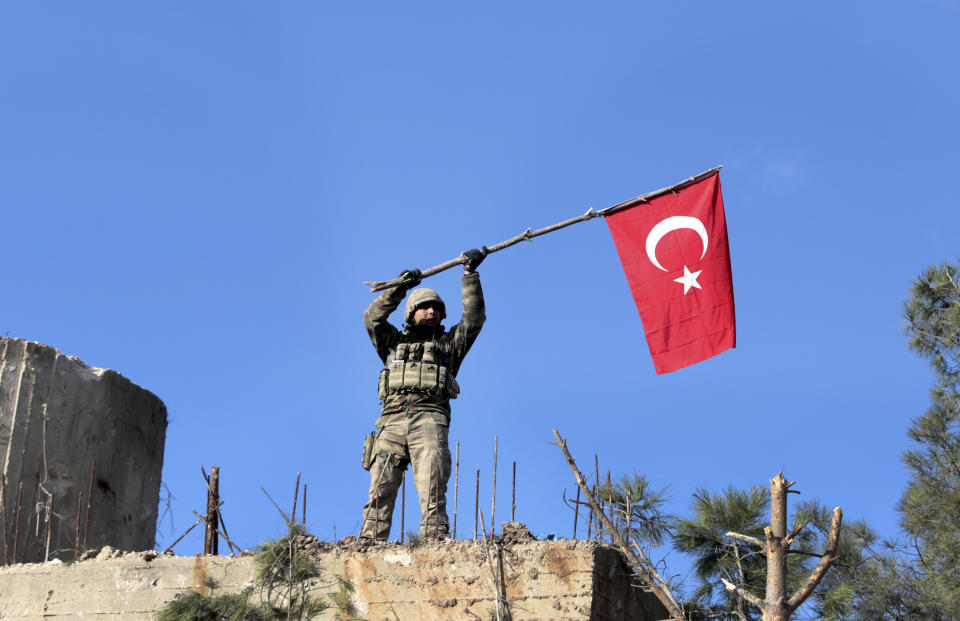 FILE -- In this Sunday, Jan. 28, 2018 file photo, a soldier waves a Turkish flag as Turkish troops secure Bursayah hill, which separates the Kurdish-held enclave of Afrin from the Turkey-controlled town of Azaz, Syria. The planned U.S. troop withdrawal opens a void in the north and east of Syria, and the conflicts and rivalries among all the powers in the Middle East are converging to fill it. (AP Photo, File)