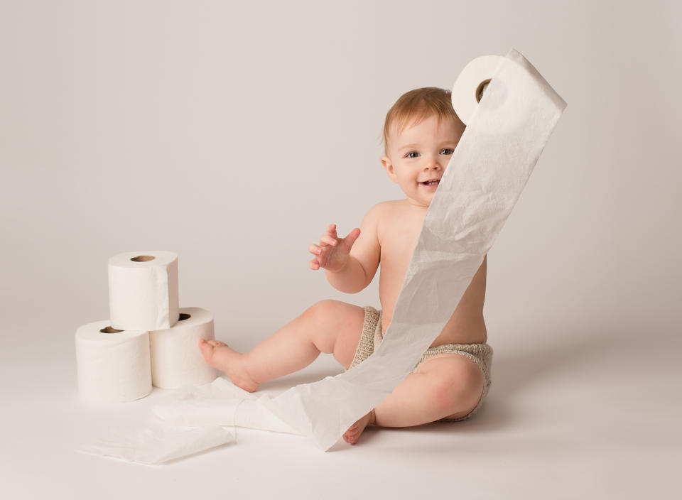 A baby playing with a roll of toilet tissue.