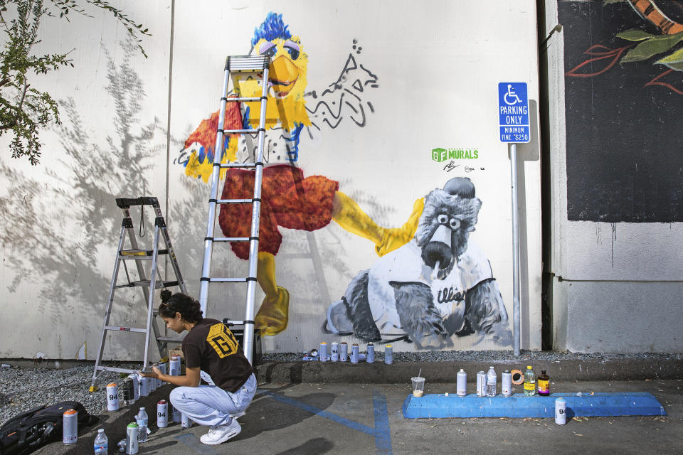 Ground Floor Murals artist Signe Ditona works on a mural of the San Diego Chicken mascot stomping on the Phillie Phanatic mascot in downtown San Diego, Monday, Oct. 17, 2022. The San Diego Padres and the Philadelphia Phillies are tied 1-1 in the baseball NL Championship Series. (Adriana Heldiz/The San Diego Union-Tribune via AP)