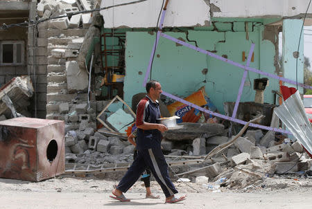 An Iraqi man walks with his son past a damaged building after the end of the battles between the Iraqi forces and Islamic State militants at their district in western Mosul, Iraq, April 30, 2017. REUTERS/Muhammad Hamed