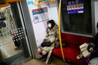 A woman wearing a protective face mask, following an outbreak of the coronavirus disease (COVID-19), rests as she travels inside a train in Tokyo