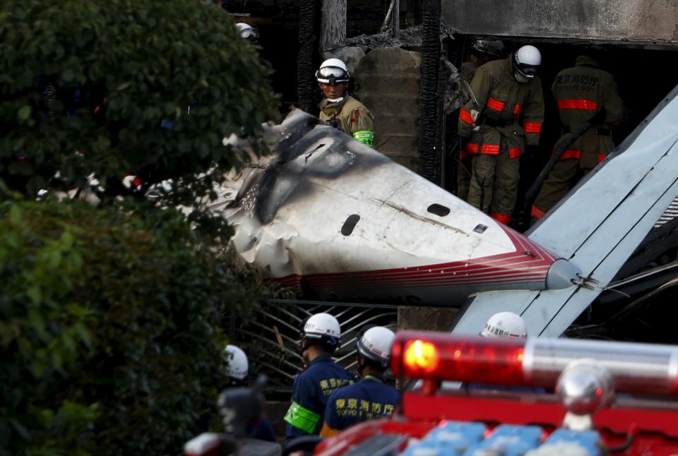 A firefighter looks at the tail section of a small airplane as he removes wreckage and debris at the site where the light plane went down in a residential area and burst into flames, in Chofu