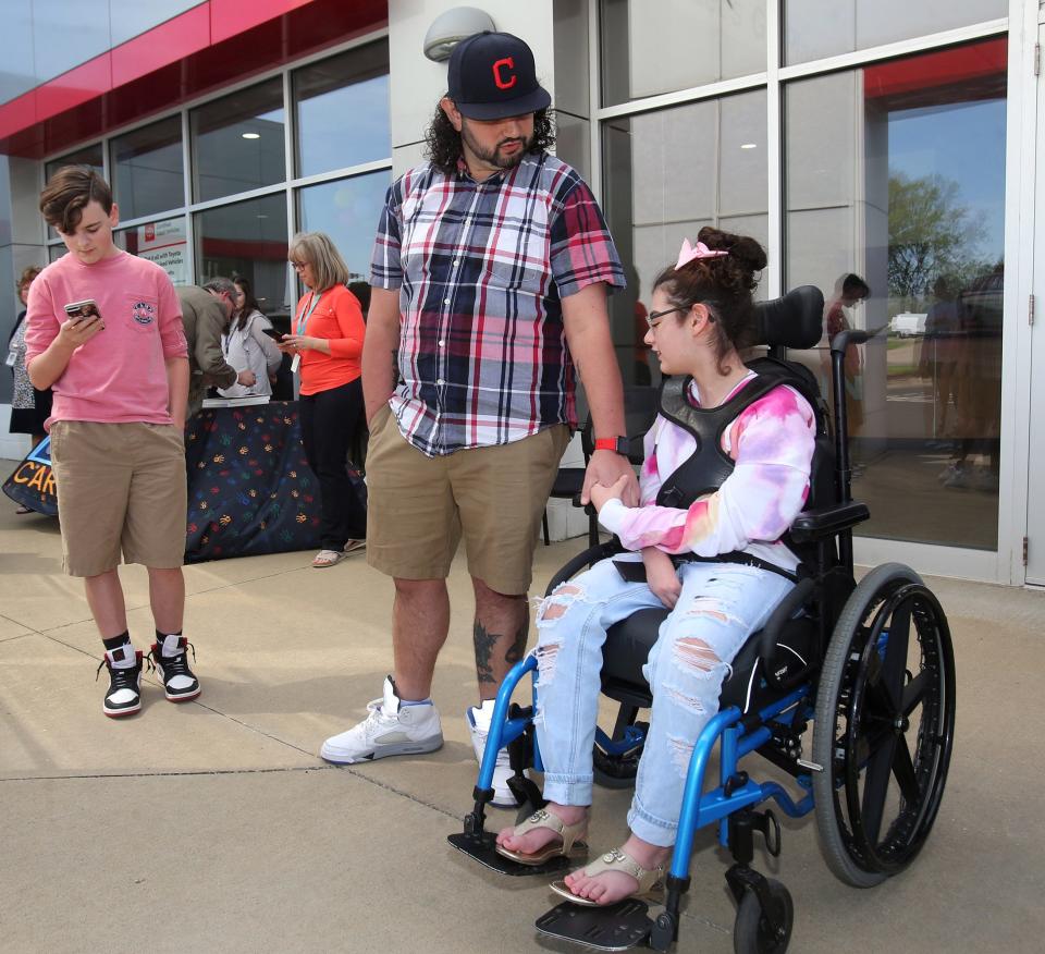 Sam McClure holds the hand of his daughter, Miah, as they wait to get a first look at her new adaptive tricycle that was presented this week to the Hoover High student at Cain Toyota-BMW in Jackson Township. At left is Miah's brother, Joey.