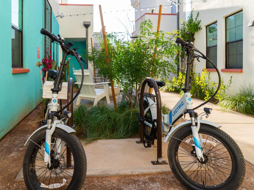 Culdesac Tempe: Two Electric Bikes parked in a floral area surrounded by white and blue buildings