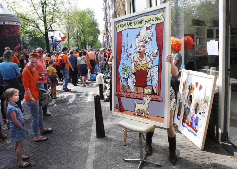 A woman poses as a young girl looks on at the annual free market during festivities marking King's Day in Amsterdam, Netherlands, Saturday, April 26, 2014. The Dutch celebrate the first ever King's Day, a national holiday held in honor of the newly installed monarch, King Willem Alexander. King's Day replaces the traditional Queen's Day. (AP Photo/Margriet Faber)