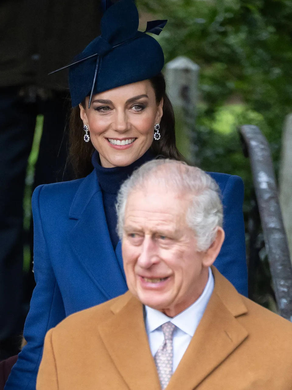 Kate Middleton in a blue coat dress walking behind King Charles in a beige coat