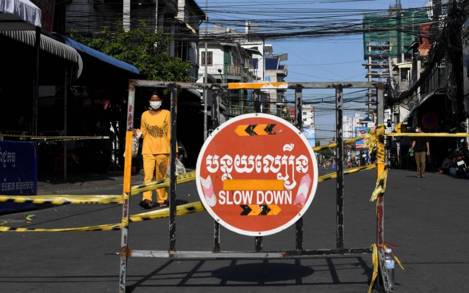A woman carries food along a street past a barricade set up in a neighbourhood due to lockdown restrictions introduced to try to halt a surge in cases of the Covid-19 coronavirus in Phnom Penh -  TANG CHHIN SOTHY / AFP