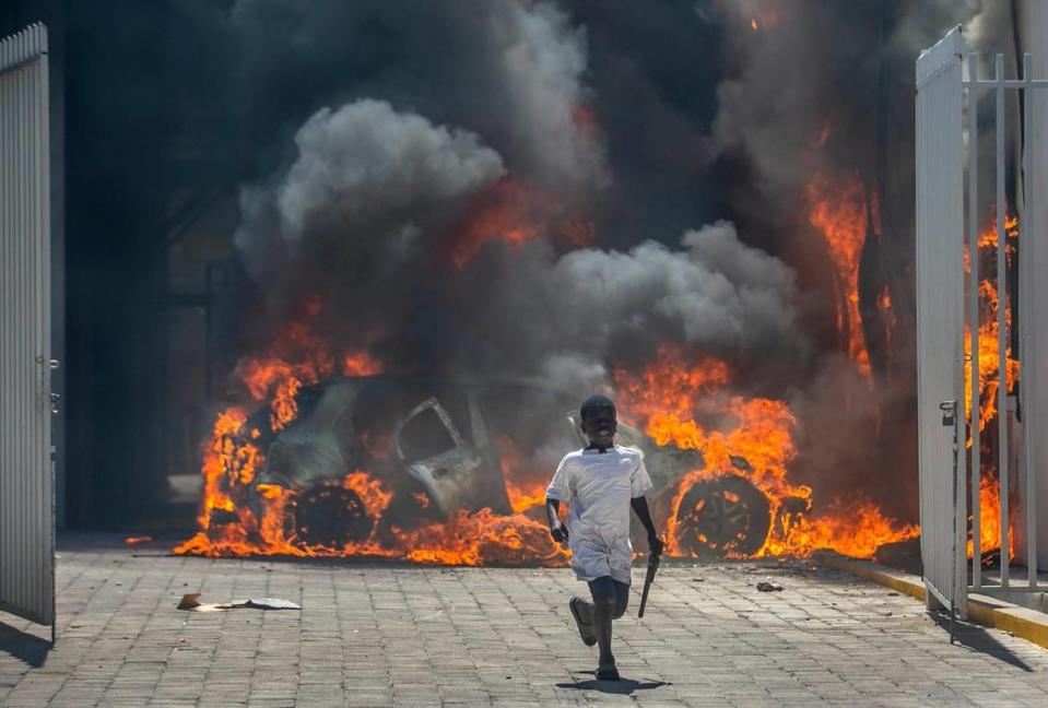 A boy runs out from the Nissan auto dealership set ablaze during a protest in Port-au-Prince, Haiti, Wednesday, March 17, 2021. The protests started when officers and police academy cadets marched toward police headquarters to demand that the bodies of several officers killed during a raid last week on the Village of God shantytown be recovered from the gang still holding them. Dieu Nalio Chery/AP