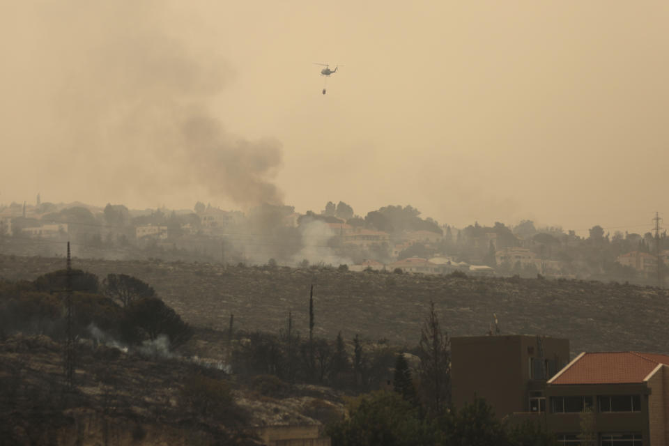 A helicopter drops water onto an advancing wildfire, in the town of Damour, just over 15km (9 miles) south of Beirut, Lebanon, Tuesday, Oct. 15, 2019. Strong fires spread in different parts of Lebanon forcing some residents to flee their homes in the middle of the night as the flames reached residential areas in villages south of Beirut. (AP Photo/Hassan Ammar)