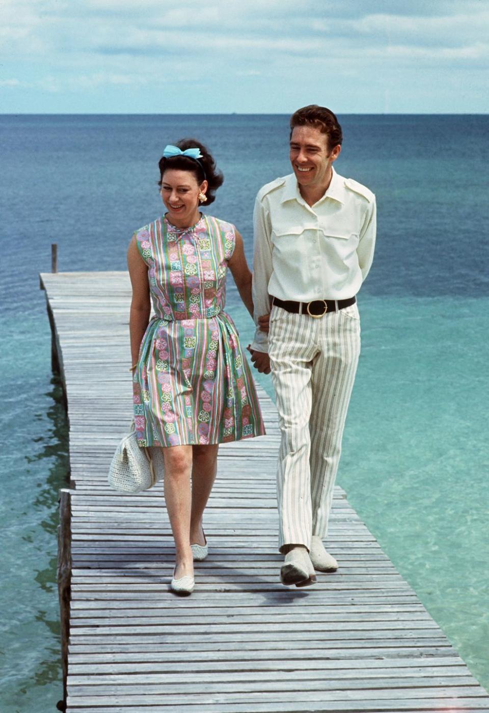 <p>Princess Margaret, wearing a patterned dress and a blue hair bow, walks with her husband the Earl of Snowdon on a pontoon in the Bahamas in 1967.</p>