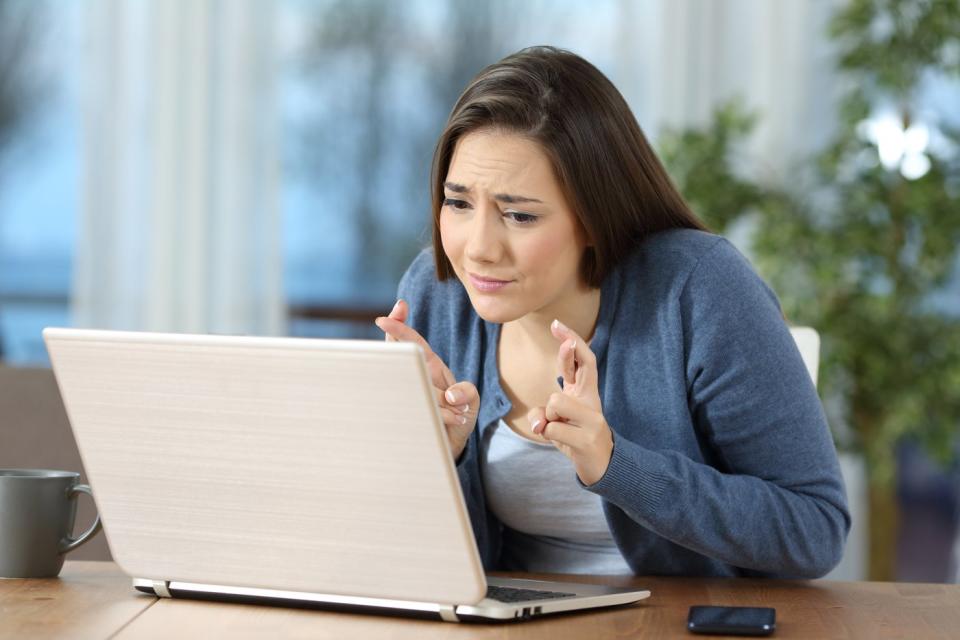 A person holding crossed fingers while looking at a laptop.