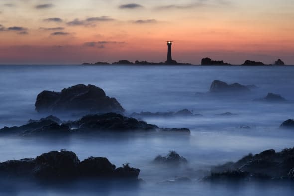 Last light over Hanoix Lighthouse creating a misty, eery view of the coastline near Hanoix in Guernsey.