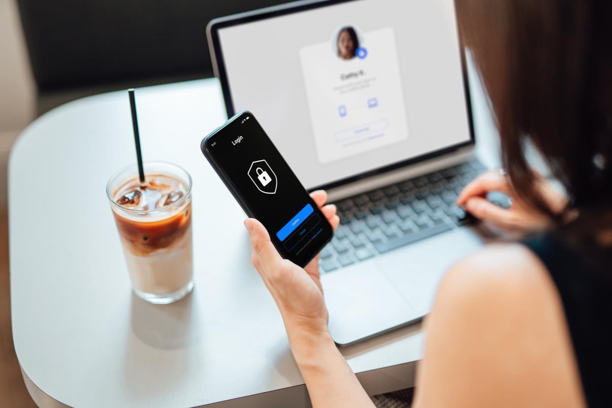 Over the shoulder view of young woman using laptop, logging in online banking account with digital security device at cafe. Internet security and digital privacy protection concept.