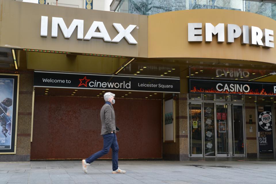 LONDON, UNITED KINGDOM - 2021/01/18: A man wearing a face mask walks past a boarded-up Cineworld, which was closed due to COVID19 pandemic at the Leicester Square in London. Venues and businesses in London are undergoing shutdown during the pandemic restrictions amid the third London lockdown. (Photo by Thomas Krych/SOPA Images/LightRocket via Getty Images)