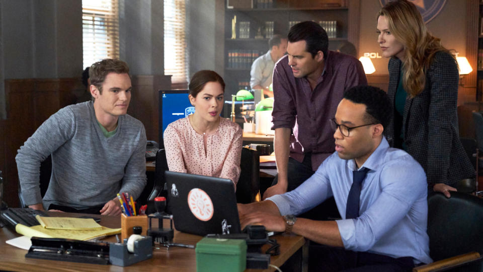 Kristoffer Polaha and Jill Wagner crowd around a laptop with co-workers in Mystery 101.