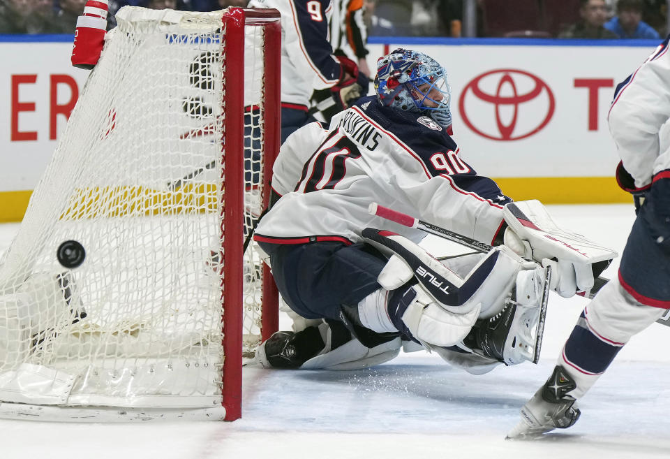 The puck deflects wide of the net behind Columbus Blue Jackets goalie Elvis Merzlikins (90) during the first period of an NHL hockey game against the Vancouver Canucks in Vancouver, British Columbia, Saturday, Jan. 27, 2024. (Darryl Dyck/The Canadian Press via AP)