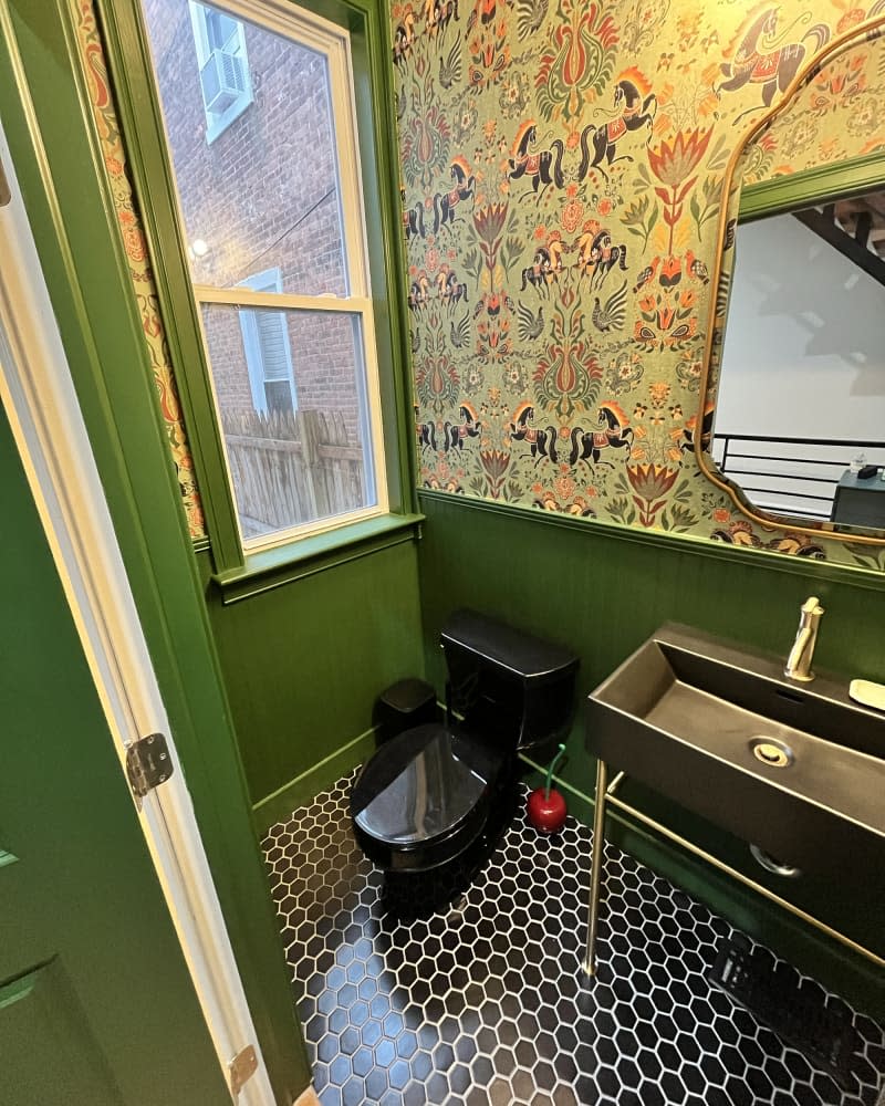 bathroom with green wainscoting, colorful horse-patterned wallpaper, gold accents, and black and white tile floor after makeover