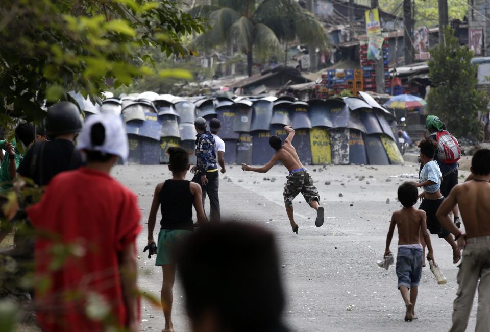 epa04044206 Filipino informal settlers throw rocks and bottles against anti-riot policemen during a demolition of shanties at Sitio San Roque in Quezon City, east of Manila, Philippines, 27 January 2014. Throwing rocks, pillboxes, and even human waste, illegal settlers barricaded the demolition team in Baranggay Bagong Pag-asa. Four residents were arrested and twelve were reported injured. Residents report receiving cash from 300 to 450 US dollar in exchange for their voluntary relocation. Earlier, hundreds of the urban poor marched to the city hall in protest of the demolition that will pave the way for the rise of a business district. EPA/DENNIS M. SABANGAN