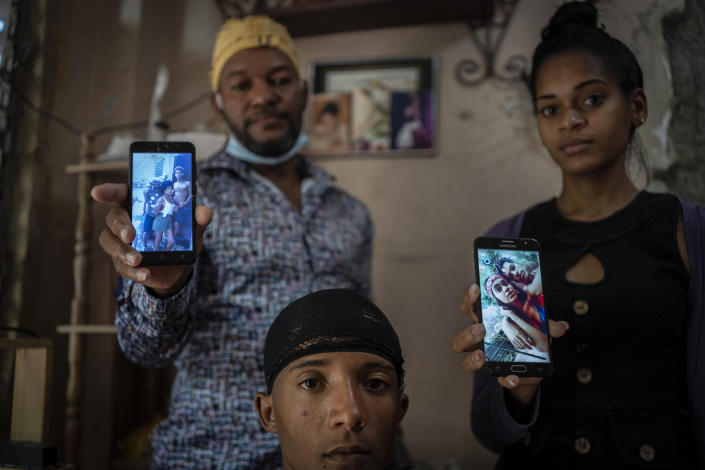 Odlanier Santiago Rodríguez, center, who was accused of participating in the recent anti-government protests and who was released after 22 days in prison, poses with his uncle Emilio Roman, left, and his daughter-in-law María Carla Milán Ramos, as they show photos of Roman´s three children who are still in prison accused of participating in the recent protets against the government, in the La Guinera neighborhood of Havana, Cuba, Wednesday, Jan. 19, 2022. Six months after surprising protests against the Cuban government, more than 50 protesters who have been charged with sedition are headed to trial and could face sentences of up to 30 years in prison. (AP Photo/Ramon Espinosa)