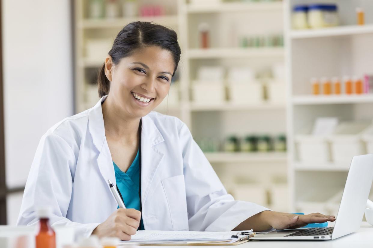 Pretty mid adult female Asian pharmacist uses a laptop at work.