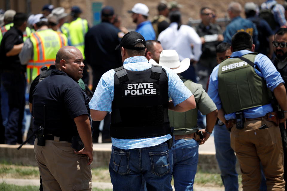 Law enforcement officials wearing protective vests are seen from behind.