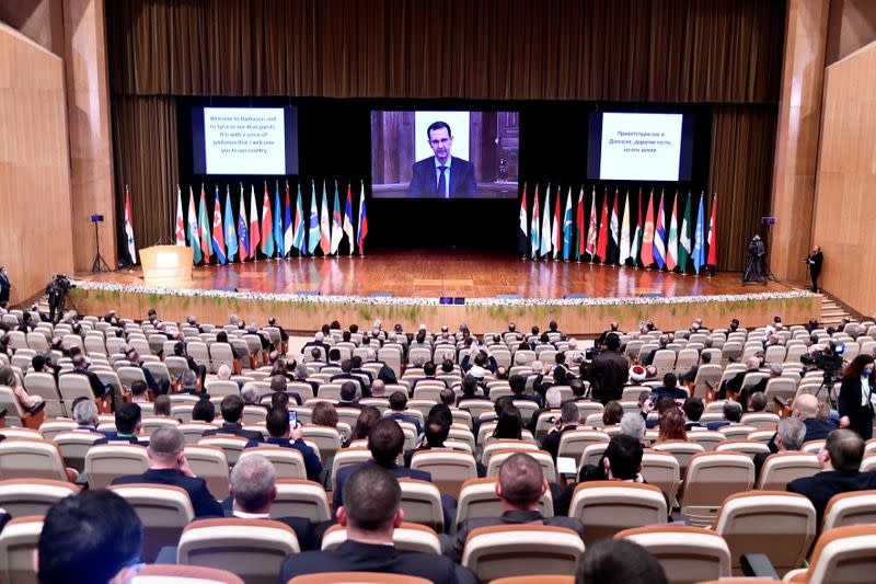 Syria's President Bashar al-Assad is seen on screen as he speaks during the international conference on the return of Syrian refugees in Damascus