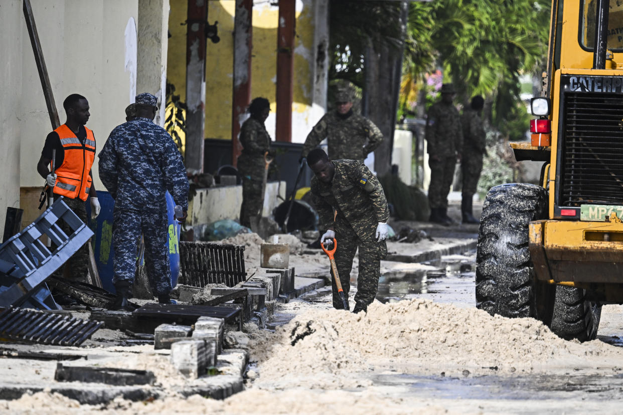 Several members of the Barbados armed forces use shovels to clear a street of sand as it gets flooded by seawater.