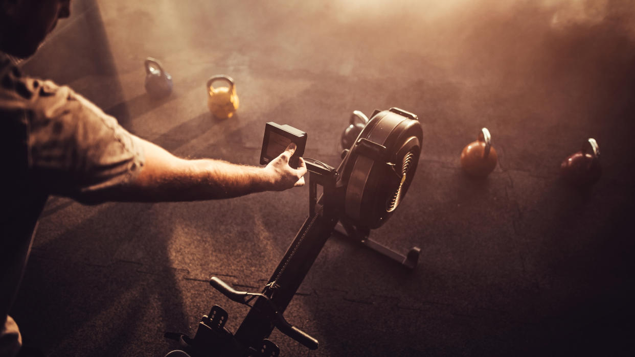  Man's arm reaches forward to press a button on the screen of a rowing machine. 