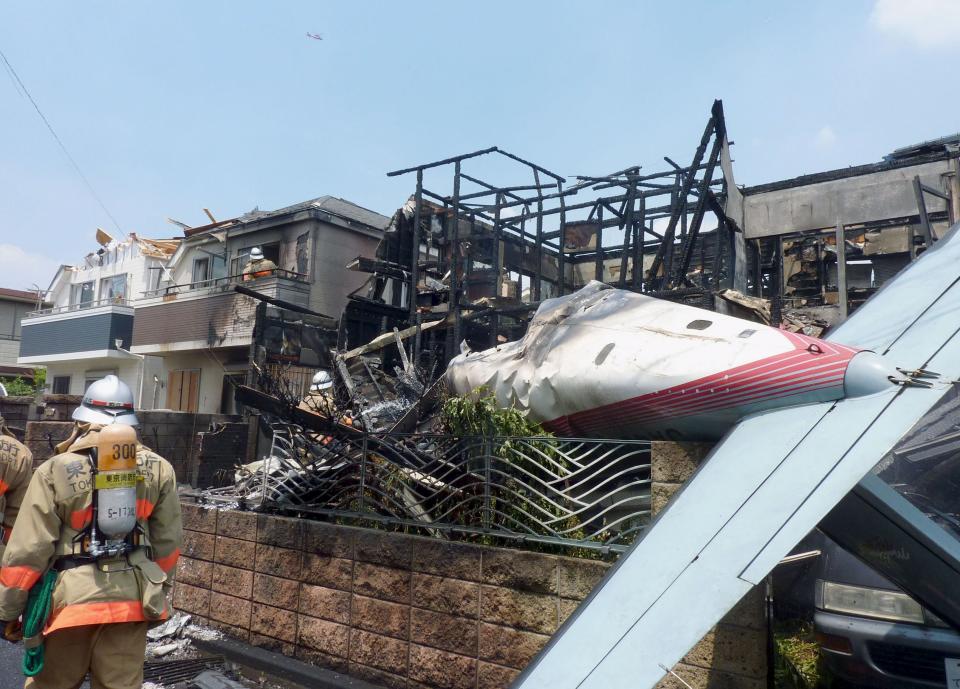 The tail section of a crashed light plane and burning house are seen after the plane went down in a residential area and burst into flames, in Chofu, outskirt of Tokyo