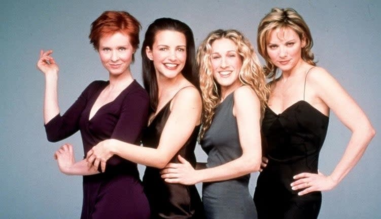 Four women from the TV show 'Sex and the City' pose together, dressed in chic evening wear