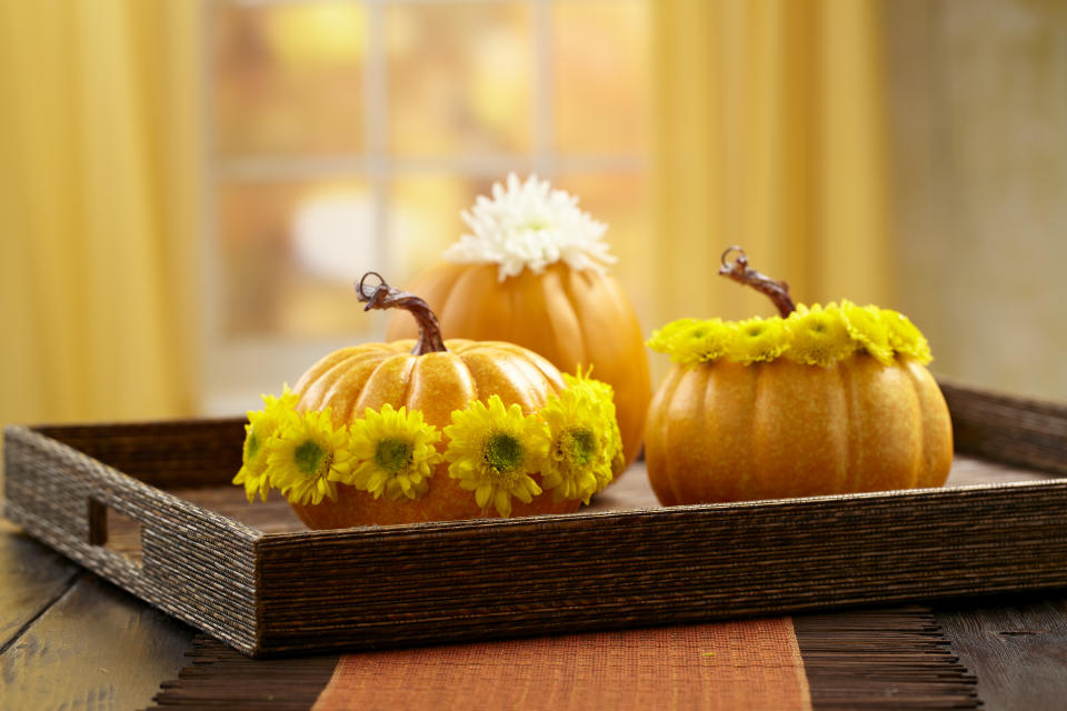 Thanksgiving holiday table display that shows three pumpkins adorned with flowers and placed on a tray on tabletop or surface 