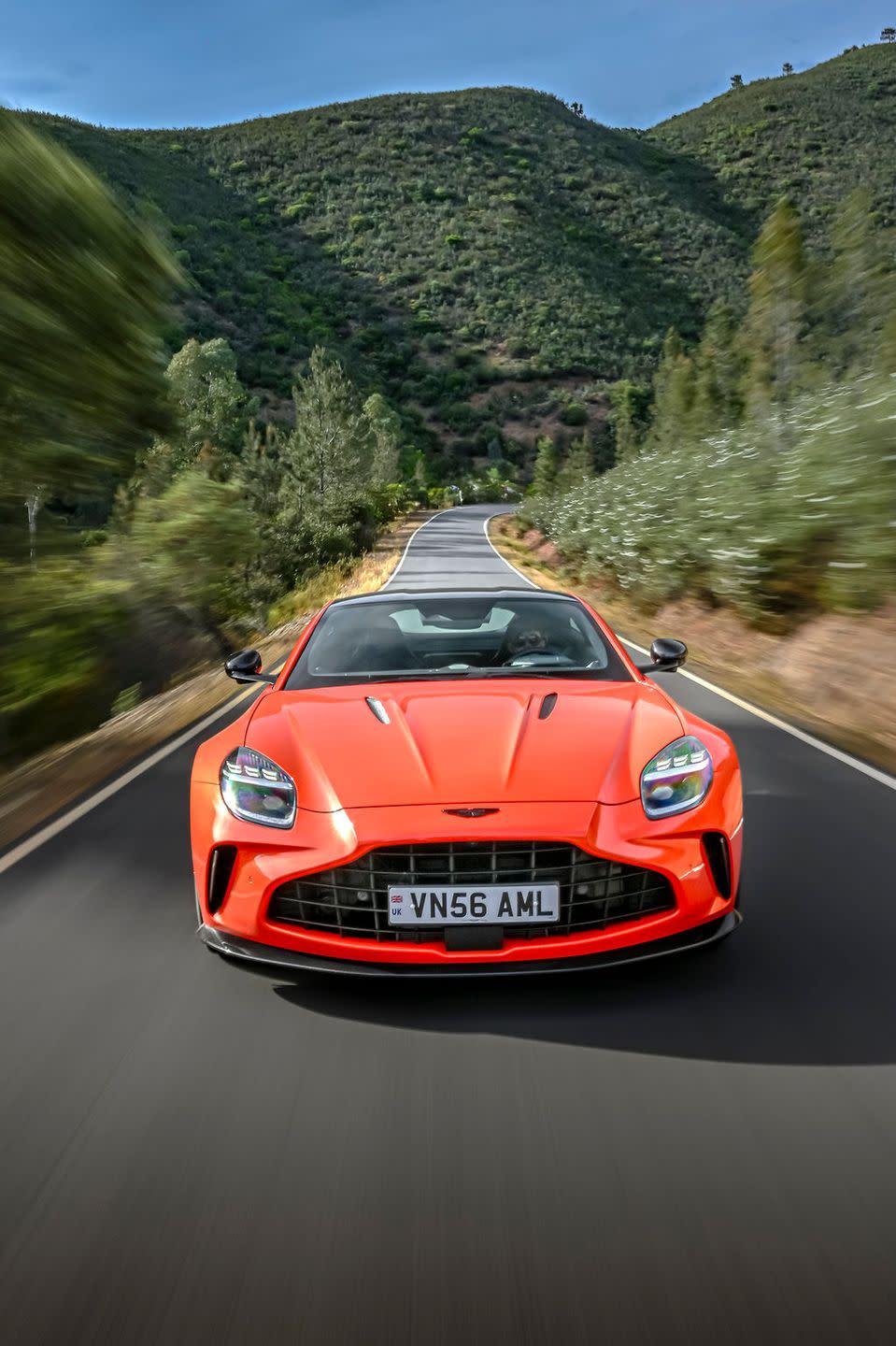 a red sports car driving on a road with trees and hills in the background