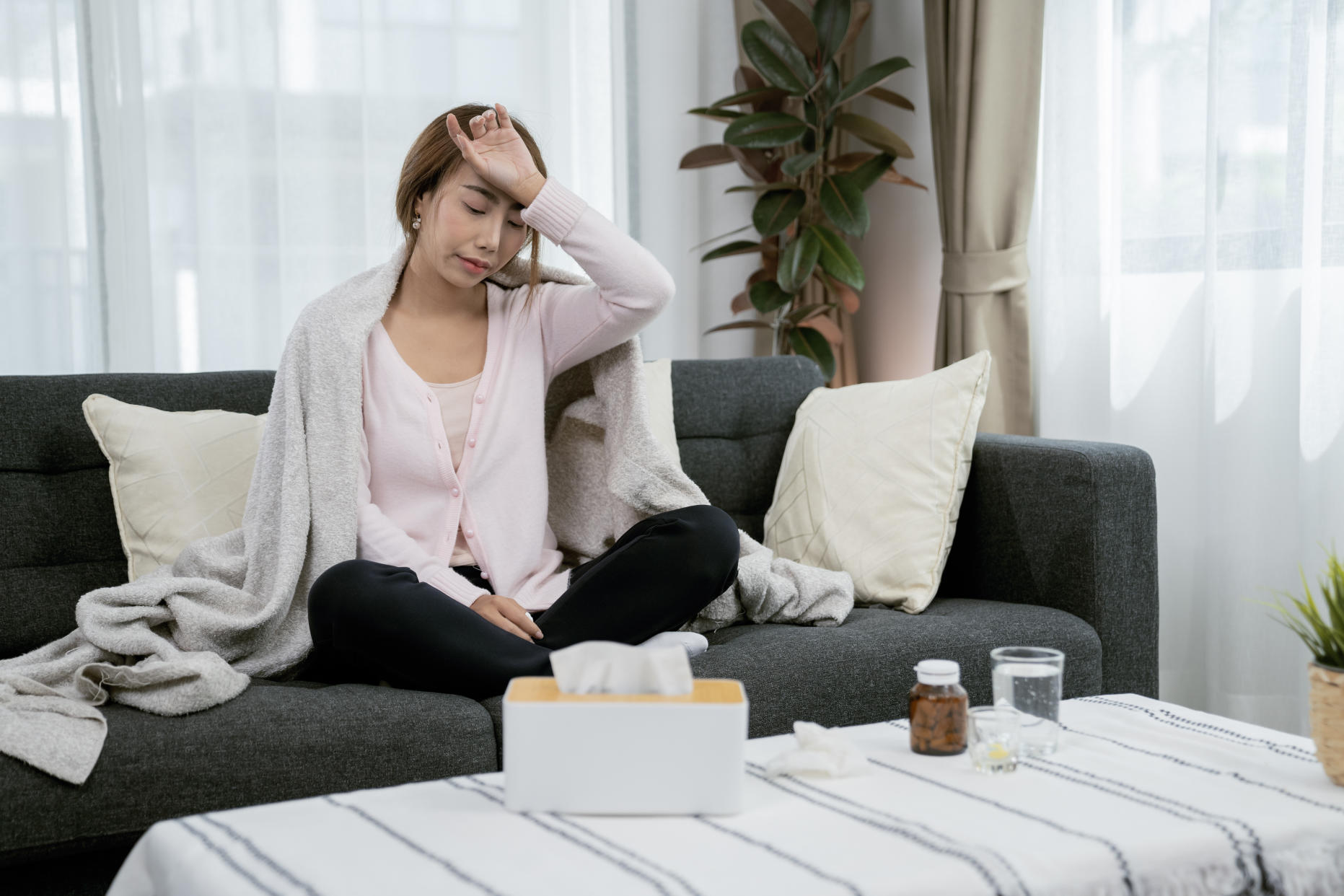 Sick woman recovering on couch with medication and tissues. (Photo via Getty Images)