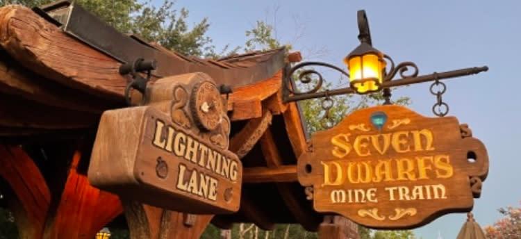 Signage for the "Seven Dwarfs Mine Train" ride and a "Lightning Lane" entrance at a theme park, with rustic wooden decorations