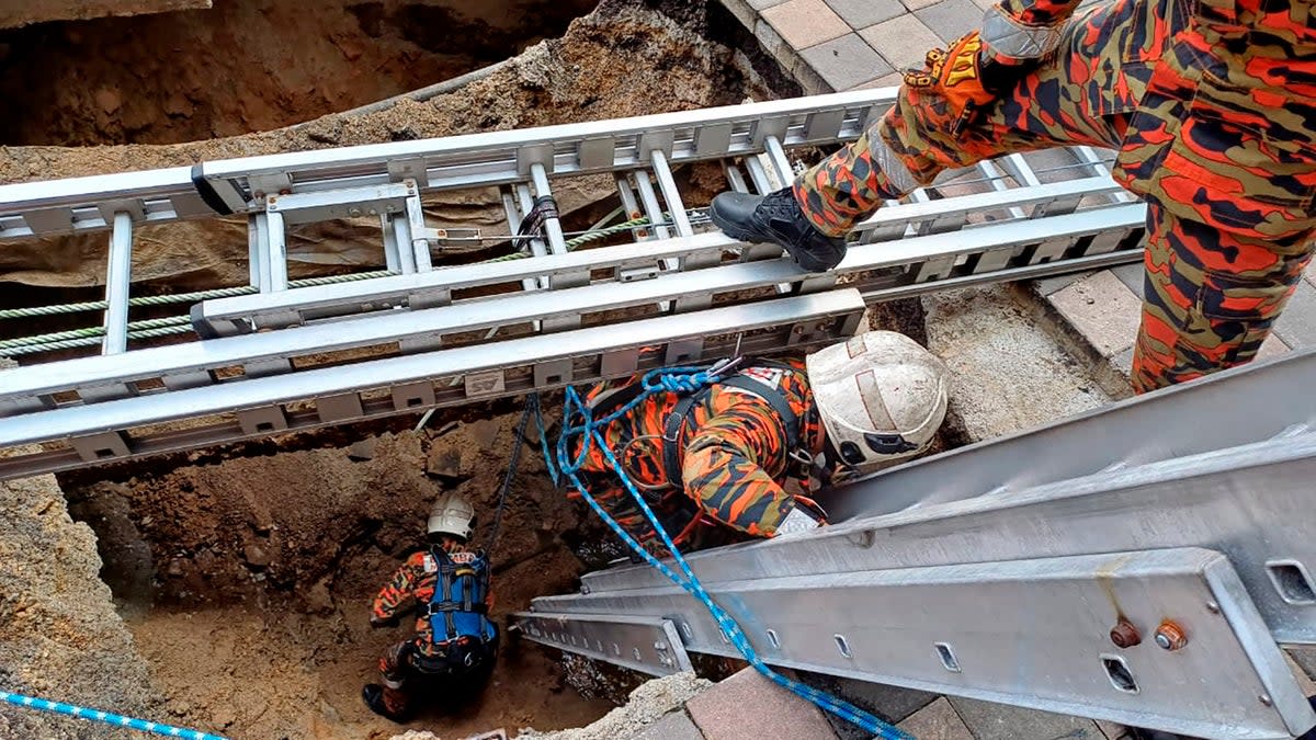 Rescue personnel enter a deep sinkhole after a woman fell into it in Kuala Lumpur (AP)