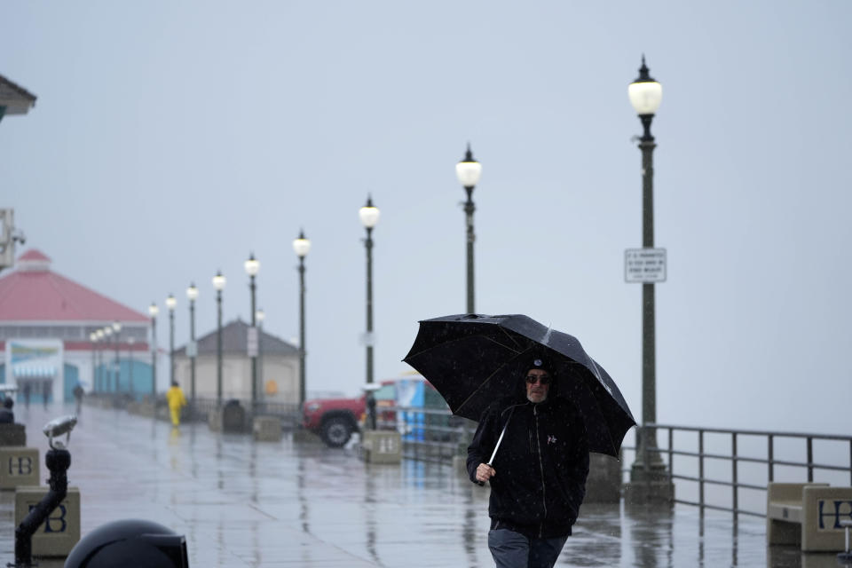 FILE - A man shields himself from the rain as he walks along the Huntington Beach Pier on Feb. 6, 2024, in Huntington Beach, Calif. California's current rainy season got off to a slow start but has rebounded with recent storms that have covered mountains in snow and unleashed downpours, flooding and mudslides. The water content of the vital Sierra Nevada snowpack has topped 80% of normal to date while downtown Los Angeles has already received more than an entire year's average annual rainfall. (AP Photo/Marcio Jose Sanchez, File)