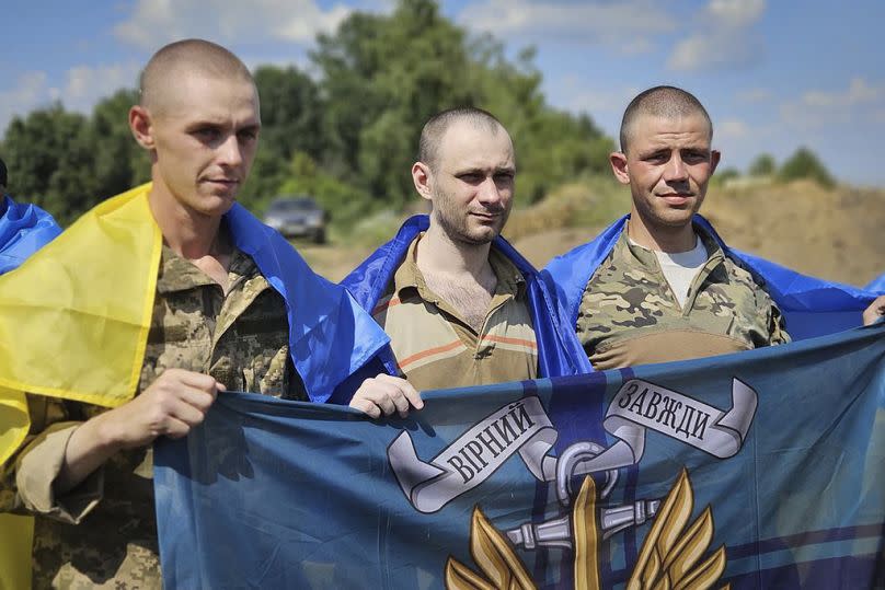 Prisioneros de guerra ucranianos sostienen la bandera de los marines mientras posan para una foto tras un intercambio de prisioneros en un lugar no revelado de Ucrania.