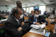 Senators Omar Aziz, sitting left, and Eduardo Braga, right, read a part of a report by a Senate commission that investigated the government's management of the COVID-19 pandemic at the Federal Senate in Brasilia, Brazil, Wednesday, Oct. 20, 2021. The commission formally presented a report recommending President Jair Bolsonaro be indicted on criminal charges for allegedly bungling Brazil's response to pandemic and pushing the country's death toll to second-highest in the world. (AP Photo/Eraldo Peres)