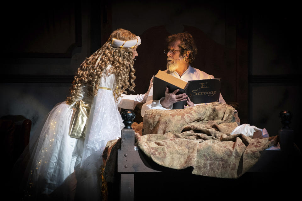 This 2018 photo provided by High Point Community Theatre in High Point, N.C., shows a scene from the 2018 production of "Ebenezer Scrooge." Shown here, The Ghost of Christmas Past, played by Courtney Lowe, takes Ebenezer Scrooge, played by Jim Freeman, on a journey through the pivotal points of his life. For many, community plays are a holiday tradition. (Brad McMillan/High Point Community Theatre via AP)