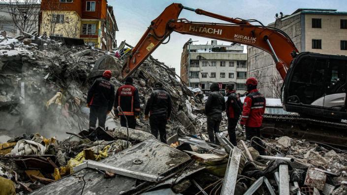 Los trabajadores observan cómo una excavadora clasifica los escombros después del terremoto en Malatya, Turquía.