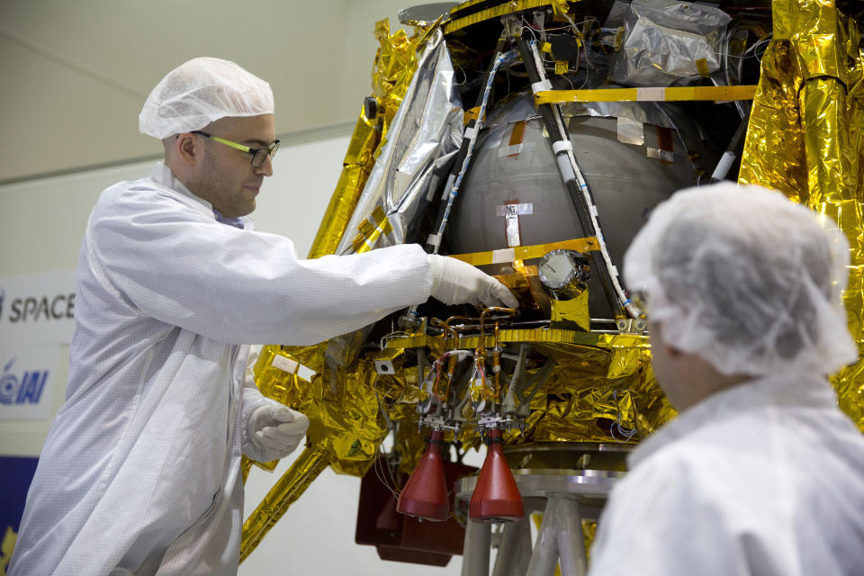 SpaceIL co-founder Yonatan Winetraub, left, inserts a time capsule into the SpaceIL lunar module, an unmanned spacecraft, that is on display in a special "clean room" where the space craft is being developed, during a press tour of their facility near Tel Aviv, Israel, Monday, Dec. 17, 2018. SpaceIL and the state-owned Israel Aerospace Industries plan to launch their unmanned spacecraft to the moon early in 2019. (AP Photo/Ariel Schalit)